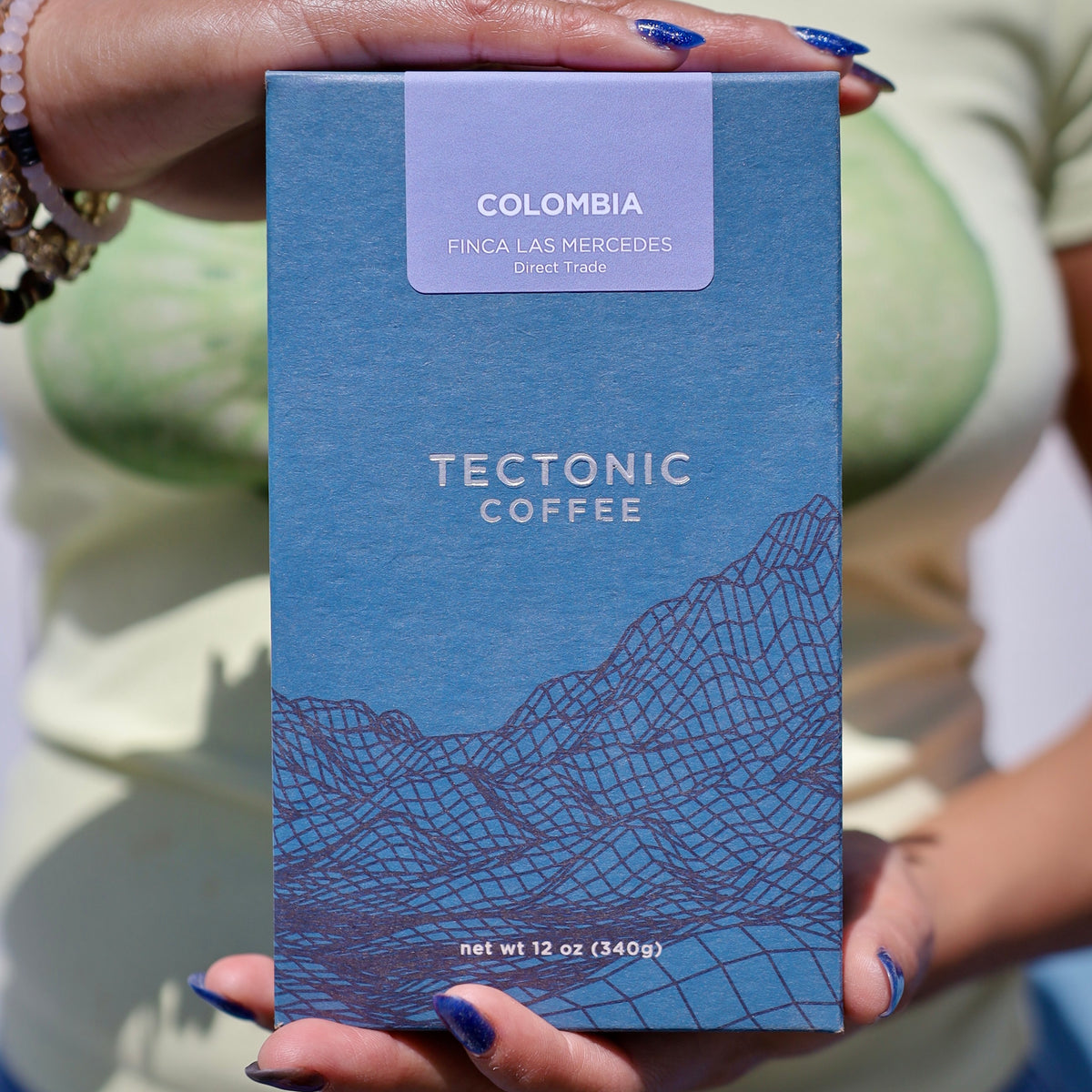 Hands holding a 12 oz box of Tectonic Coffee Colombia Finca Las Mercedes.