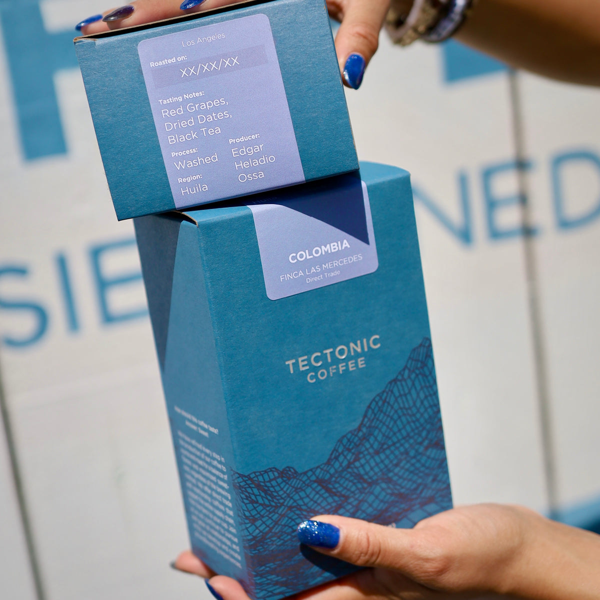 Hands holding two Colombia Finca Las Mercedes coffee boxes, showing the producer and tasting notes.