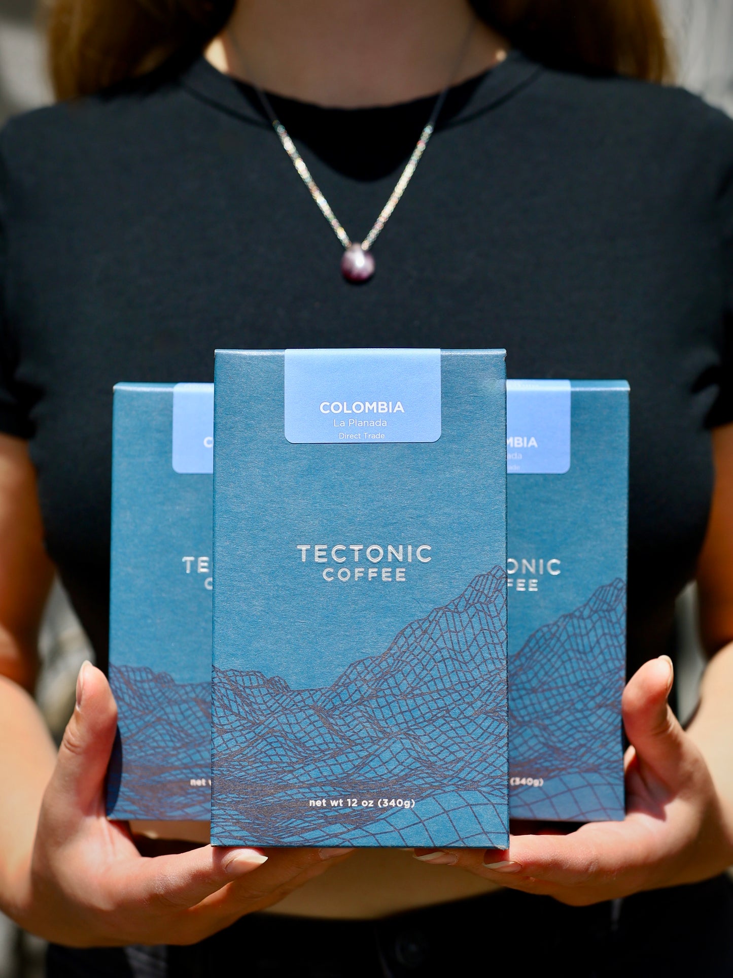 Person holding three blue Tectonic Coffee packages