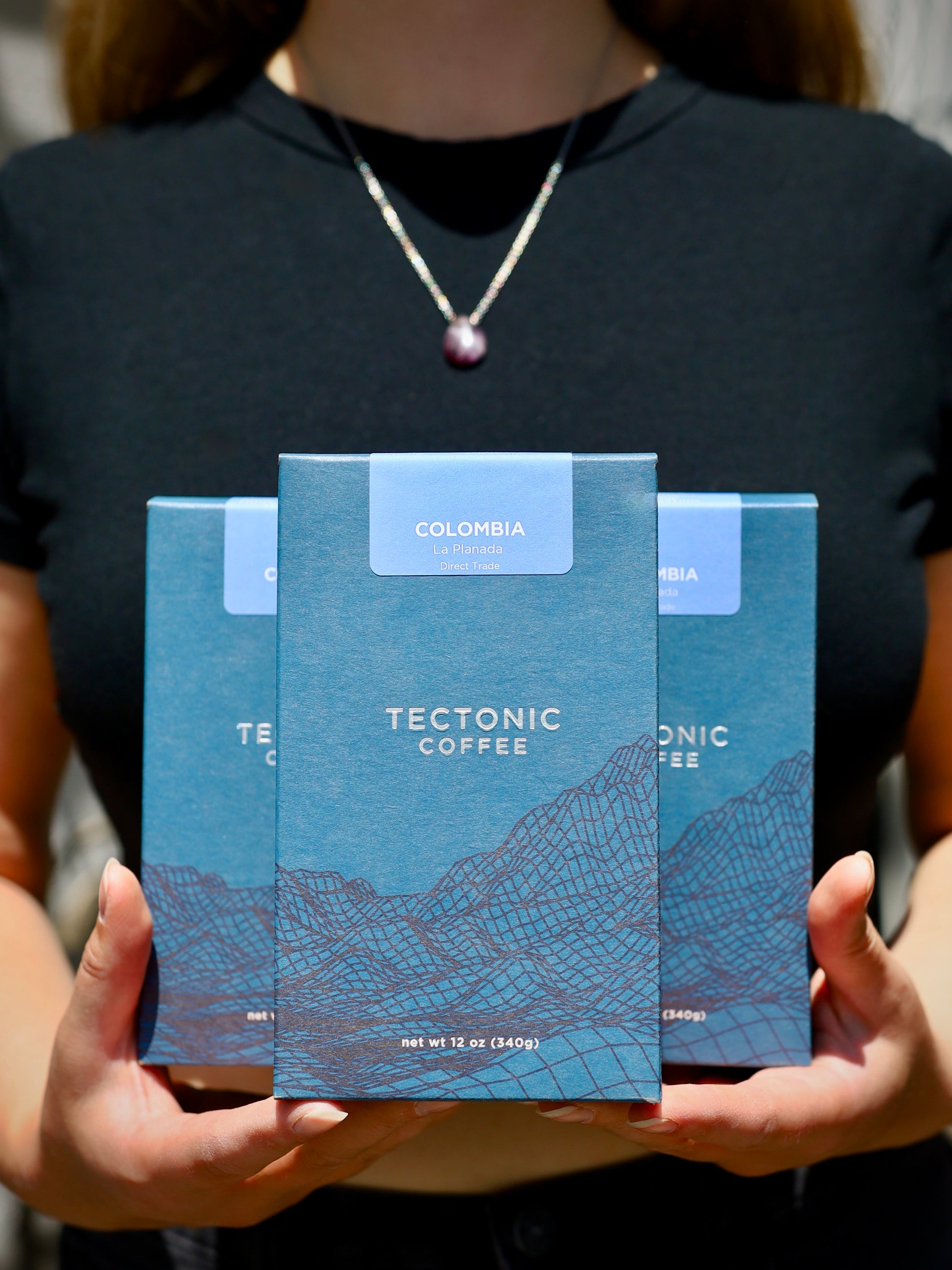 Person holding three blue Tectonic Coffee packages