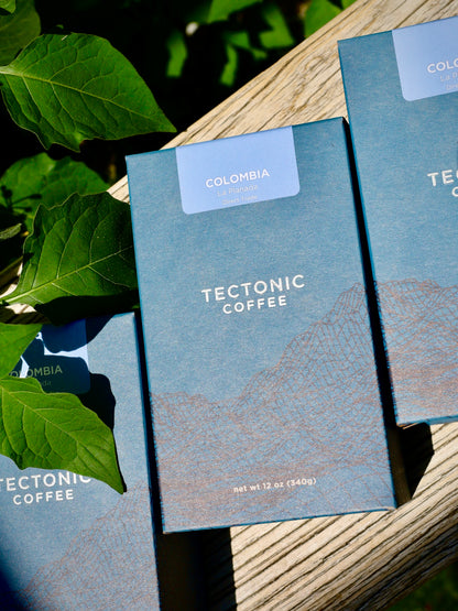 Tectonic Coffee packages on a wooden surface with green leaves in the background