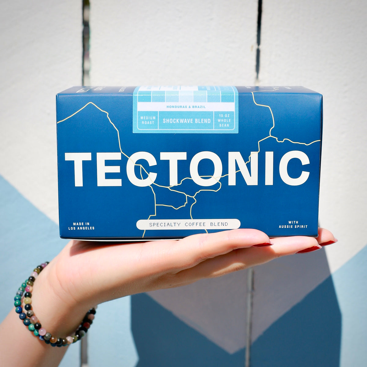Tectonic Coffee Shockwave Blend 10oz box held in one hand against a light wall; whole bean packaging shown
